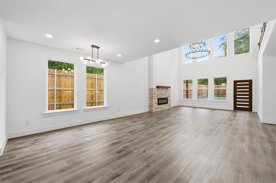 Unfurnished living room featuring a chandelier, healthy amount of natural light, a fireplace, light wood finished floors, and recessed lighting