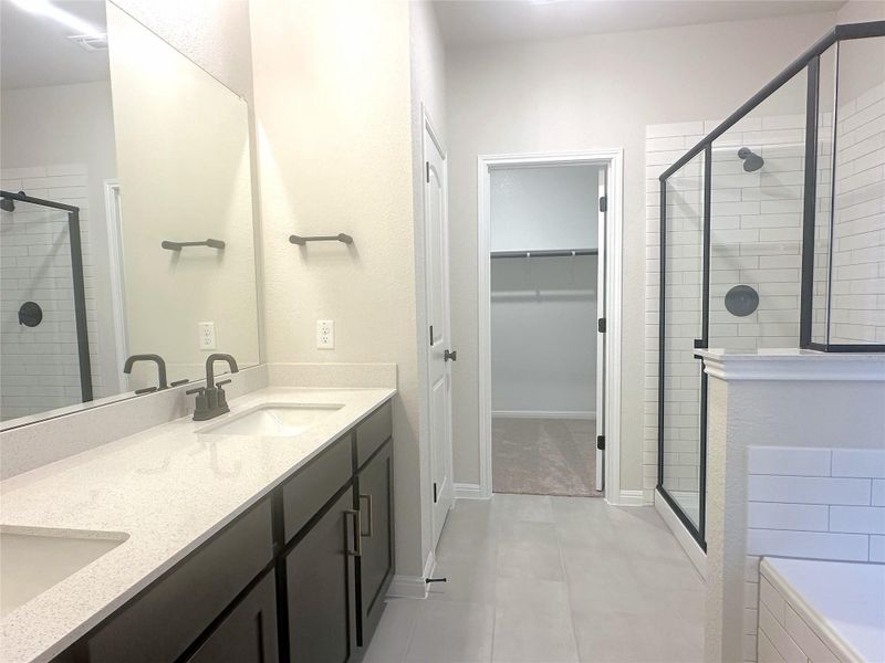 Full bath featuring a stall shower, a spacious closet, double vanity, tile floors, and a tub to relax in