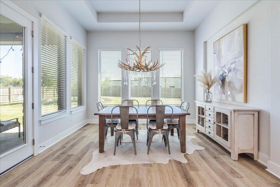 Dining space featuring a raised ceiling, hanging lights, and light wood-style flooring Dining space featuring a raised ceiling, hanging lights, and light wood-style flooring