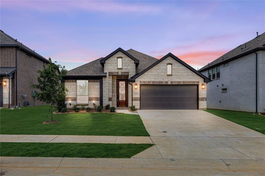 Single-story home with light stone exterior, two-car garage, and manicured front lawn at dusk Single-story home with light stone exterior, two-car garage, and manicured front lawn at dusk