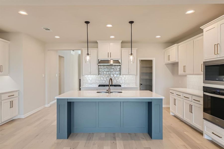 Kitchen with light hardwood / wood-style floors, stainless steel appliances, decorative light fixtures, and a center island with sink