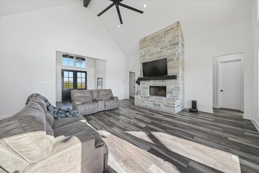 Living room with high vaulted ceiling, dark wood-style floors, a fireplace, beam ceiling, and a ceiling fan
