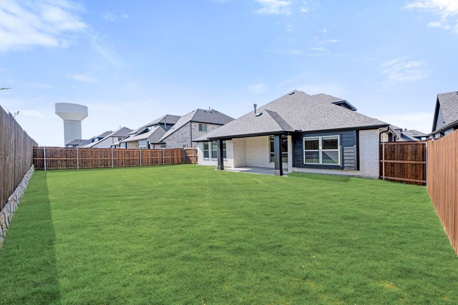 Backyard with large green lawn, wood privacy fence, and covered patio on brick home Backyard with large green lawn, wood privacy fence, and covered patio on brick home