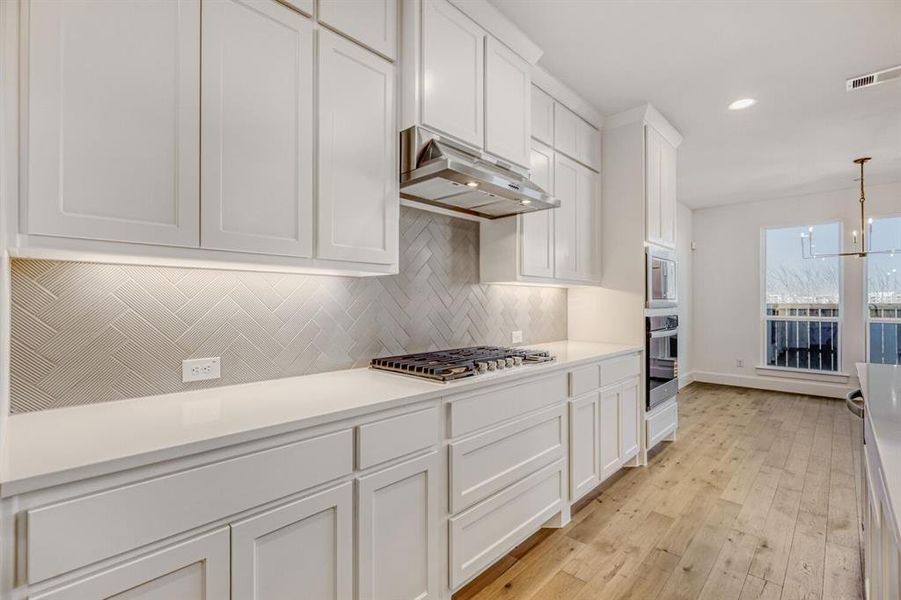 Kitchen with white cabinetry, a chandelier, light wood-style flooring, stainless steel appliances, and light stone countertops