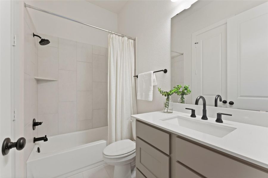 Bathroom featuring a white bathtub with subway tile surround, matte black fixtures, a built-in shower shelf, a vanity with a white countertop, and a large wall-mounted mirror