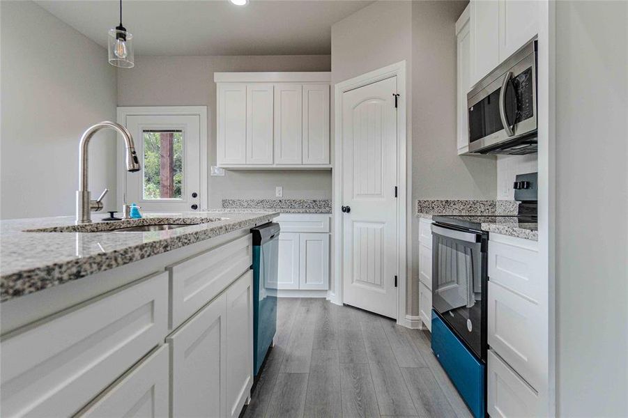 Kitchen featuring stainless steel appliances, hanging light fixtures, white cabinets, light stone counters, and light hardwood / wood-style flooring