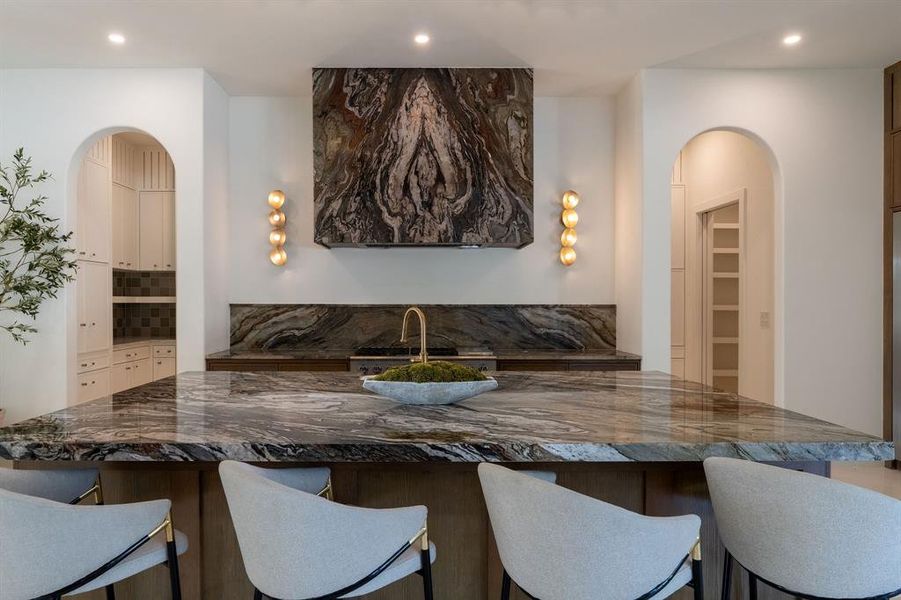 Kitchen with arched walkways, dark stone countertops, a kitchen breakfast bar, recessed lighting, and tasteful backsplash