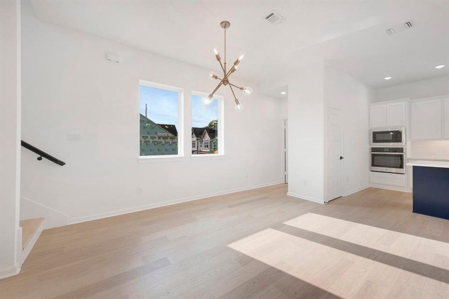 Open-concept living area featuring light wood-finish flooring, a contemporary sputnik chandelier, and two large windows