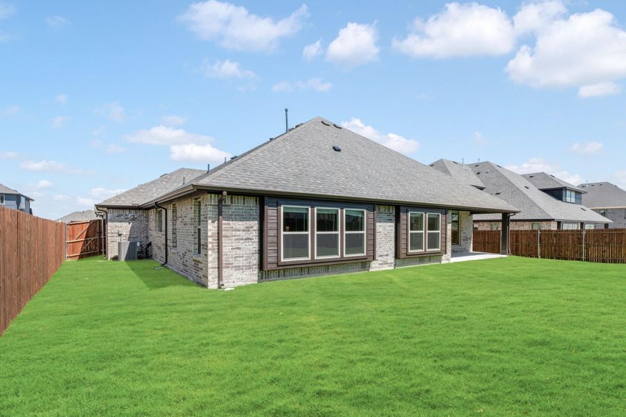 Rear view of single-story brick home with large windows, green lawn, and wood privacy fence