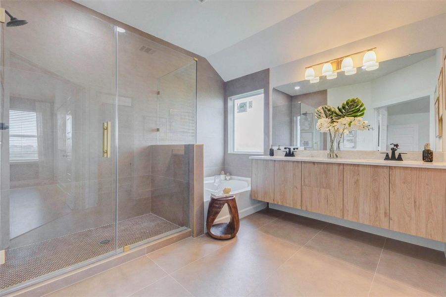 This luxurious bathroom offers a spa-like experience with a large walk-in glass shower, elegant tile finishes, and a soaking tub perfect for relaxation. The double vanity provides ample storage and counter space, while modern fixtures and lighting add a refined touch. Every detail is thoughtfully designed for both comfort and sophistication. The picture shown is from the model home with the same floor plan, Rev floor plan.