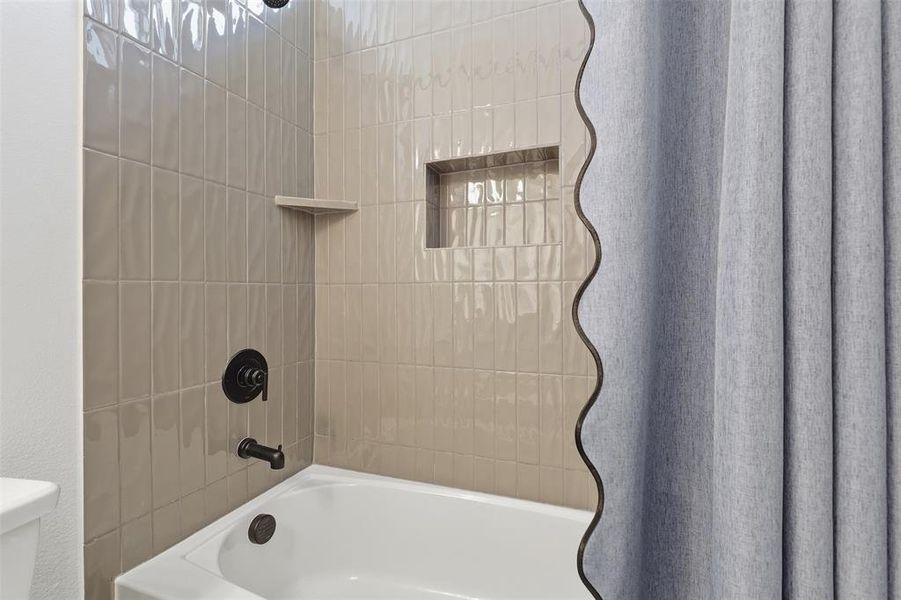 Bathtub with matte black fixtures, textured subway tile surround, recessed niche, and integrated shelf Bathtub with matte black fixtures, textured subway tile surround, recessed niche, and integrated shelf