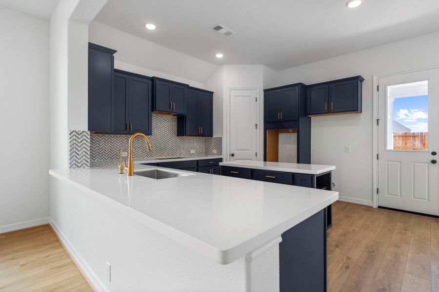 This light and bright kitchen features a large quartz island, custom stained cabinets, a large sink overlooking your family room, recessed lighting, and beautiful backsplash.