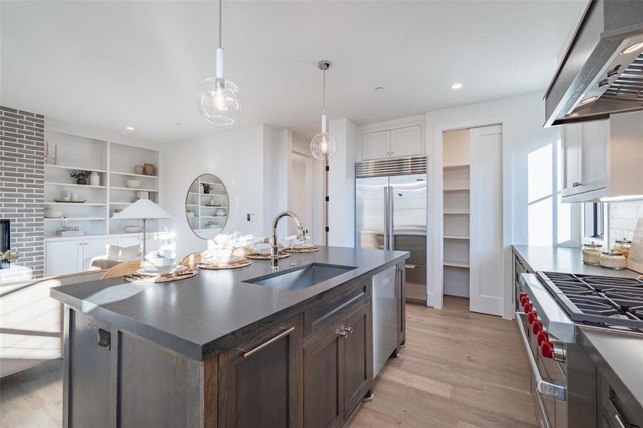 Kitchen featuring dark brown cabinets, exhaust hood, sink, white cabinetry, and an island with sink