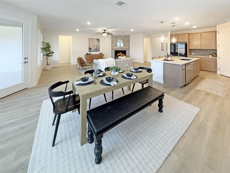 Dining room with light wood-type flooring, a ceiling fan, a warm lit fireplace, and recessed lighting