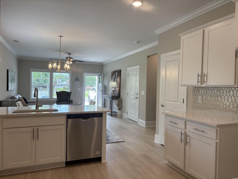 Kitchen featuring stainless steel dishwasher, a sink, light countertops, open floor plan, and tasteful backsplash