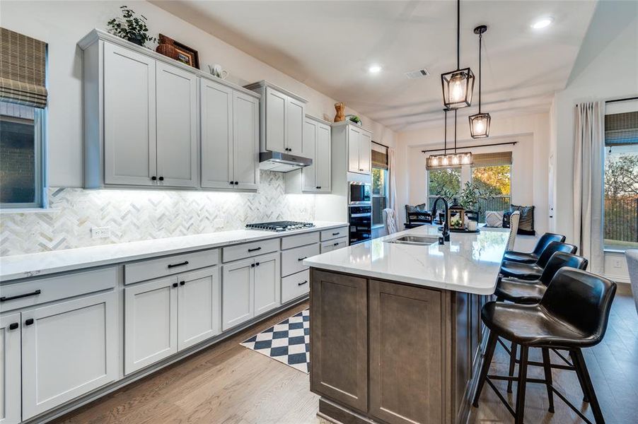 Kitchen with hanging light fixtures, a kitchen island with sink, light stone counters, a breakfast bar area, and dark brown cabinetry