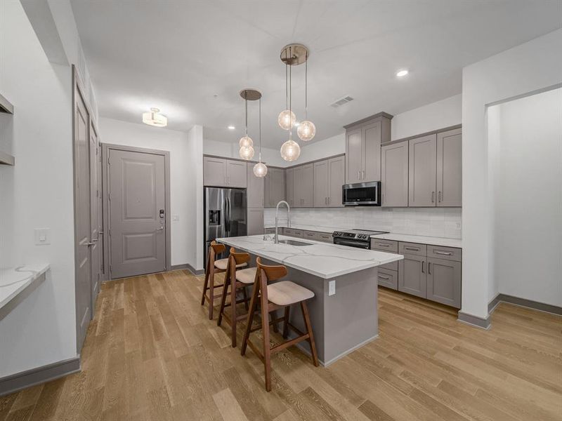 Kitchen with gray cabinets, a breakfast bar area, decorative light fixtures, a center island with sink, and tasteful backsplash