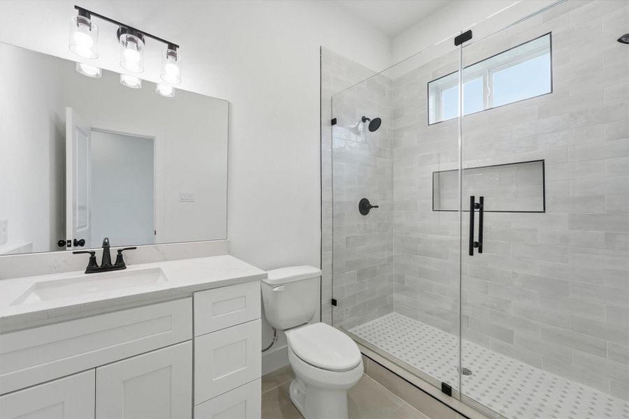 Every bath in this home is a statement. This full bath features quartz countertops, white shaker cabinetry, matte black fixtures, a frameless glass shower with large-format tile surround, built-in niche, and mosaic penny tile floor that brings a spa-like finish to everyday life. Every bath in this home is a statement. This full bath features quartz countertops, white shaker cabinetry, matte black fixtures, a frameless glass shower with large-format tile surround, built-in niche, and mosaic penny tile floor that brings a spa-like finish to everyday life.