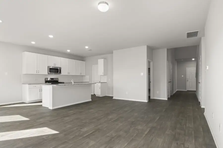 Image of a living room with dark brown wood-like flooring and light grey painted walls with an open concept kitchen