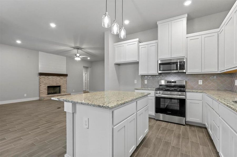 Kitchen with a fireplace, white cabinetry, pendant lighting, and stainless steel appliances