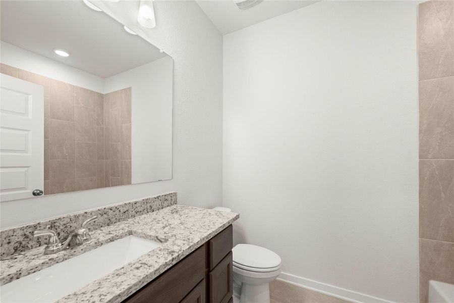 A well-appointed primary bathroom featuring a spacious granite vanity and modern toilet.