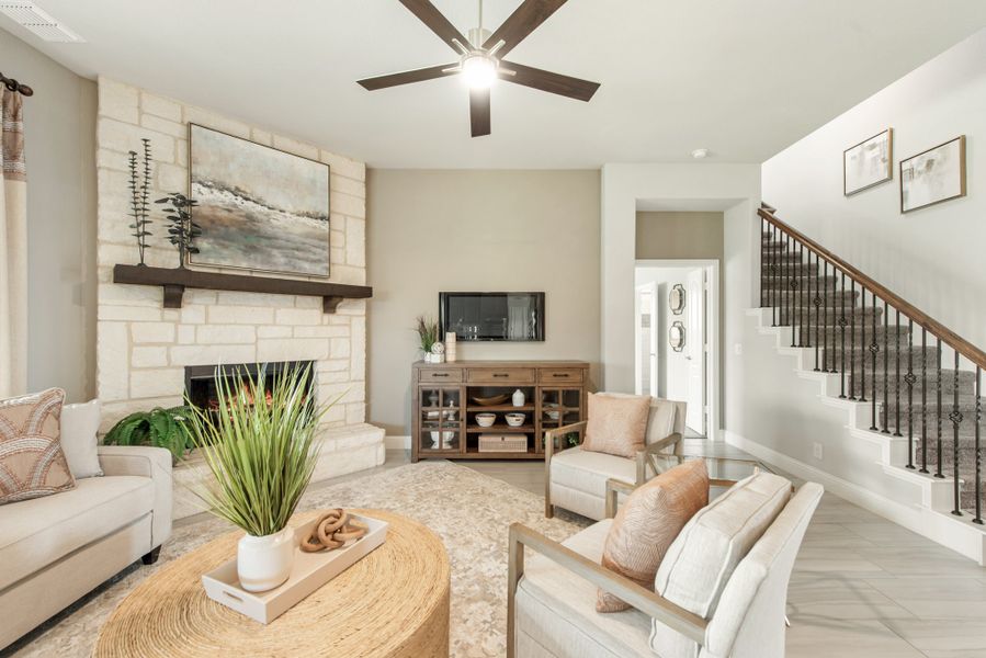 Living room with stone fireplace, ceiling fan, neutral seating, and staircase with wood and iron railing