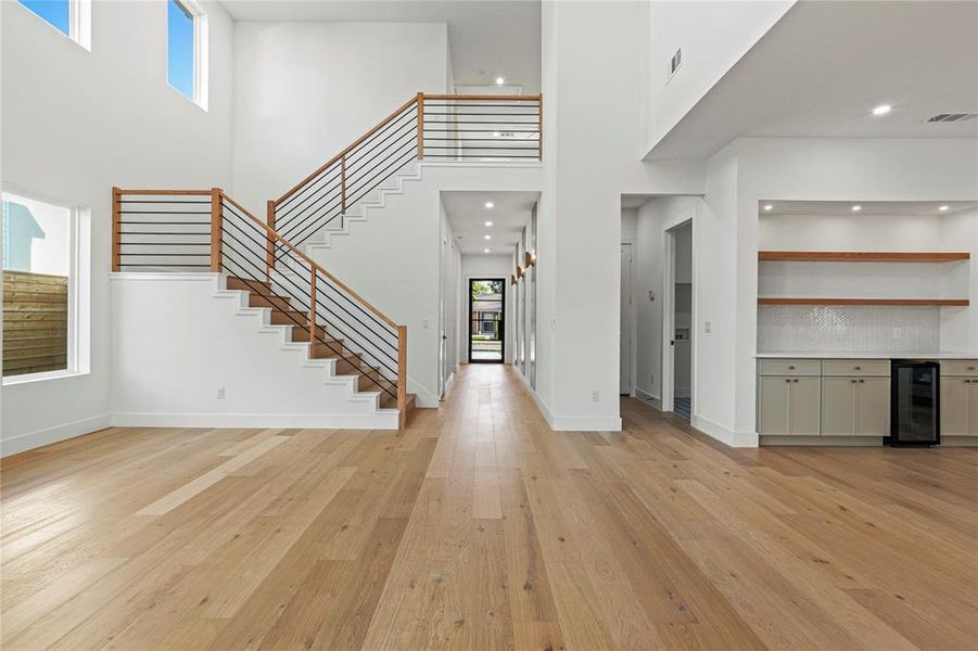 Unfurnished living room with a high ceiling, light wood-style flooring, wine cooler, stairway, and bar