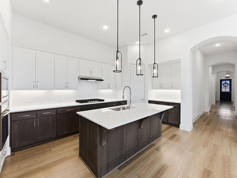 Two tone kitchen featuring two tone cabinets, arched walkways, an island with sink, a breakfast bar area, and light wood finished floors