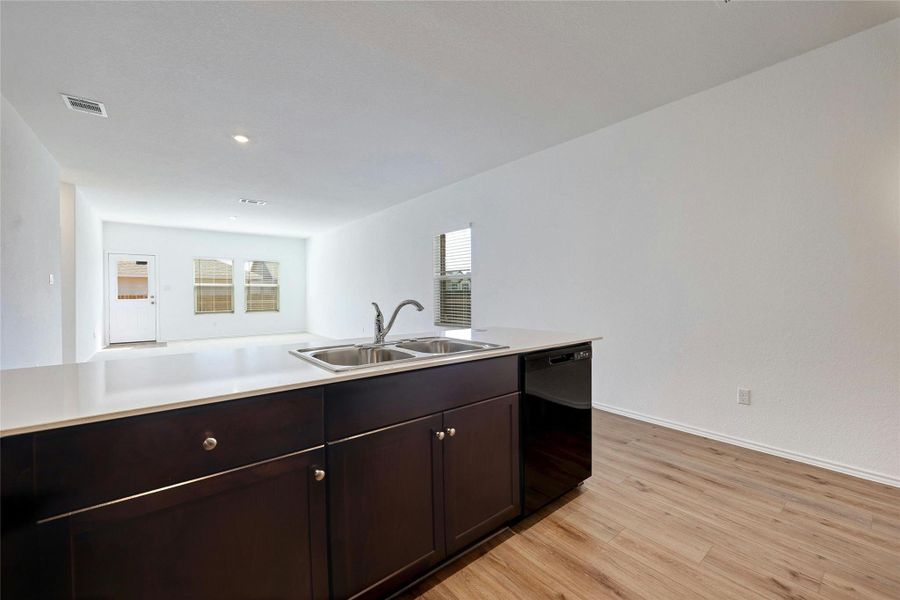 Kitchen featuring light countertops, dark wood finish cabinets, dishwasher, light wood finished floors, and recessed lighting