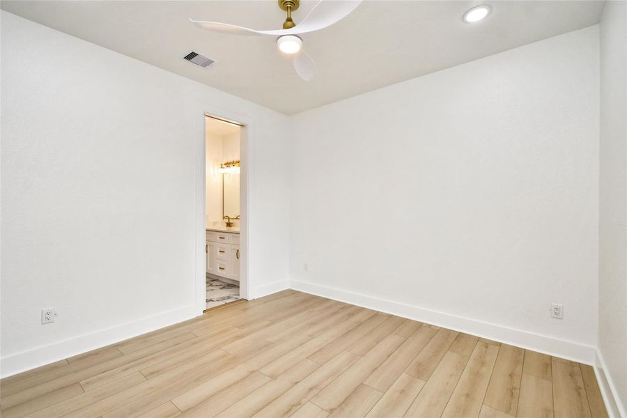 Bright and modern secondary bedroom featuring vaulted ceiling lines and a sleek aerodynamic ceiling fan. Crisp white walls and durable wood-look flooring provide a clean, contemporary aesthetic.