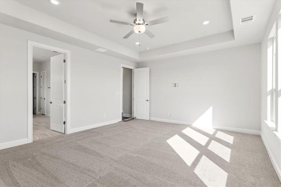 Unfurnished bedroom with light carpet, recessed lighting, a tray ceiling, and a ceiling fan