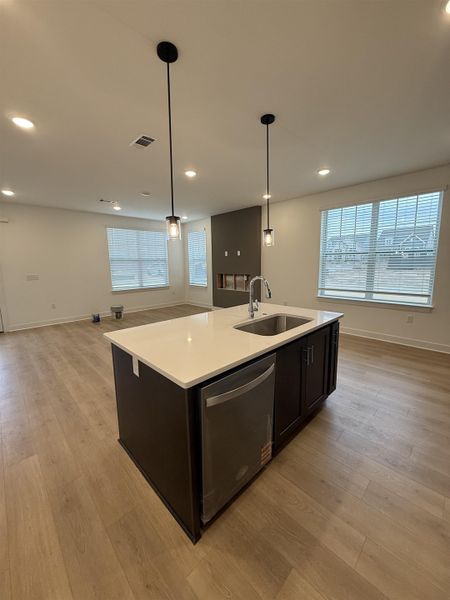 Kitchen featuring a center island with sink, dishwasher, open floor plan, pendant lighting, and light wood-style floors