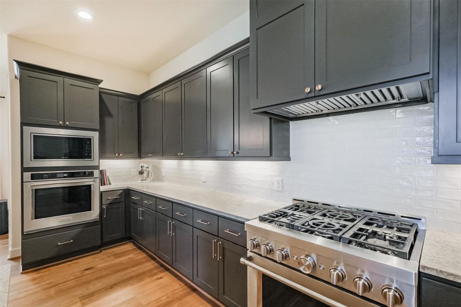 View of the gourmet kitchen featuring a beautiful backsplash and upgraded stainless appliances; including 6-burner gas range, built in stainless steel microwave, and electric oven.