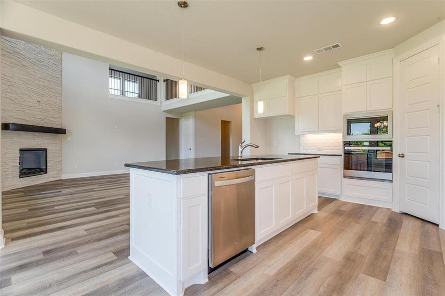 Kitchen with a fireplace, a center island with sink, stainless steel appliances, light wood-type flooring, and white cabinets