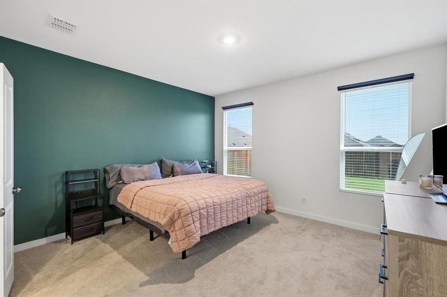 Bedroom featuring a dark teal accent wall, neutral carpeting, and two windows with blinds Bedroom featuring a dark teal accent wall, neutral carpeting, and two windows with blinds