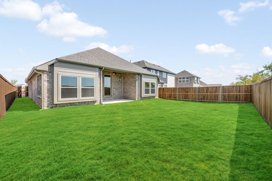Brick home rear exterior with large fenced backyard, green lawn, and covered patio