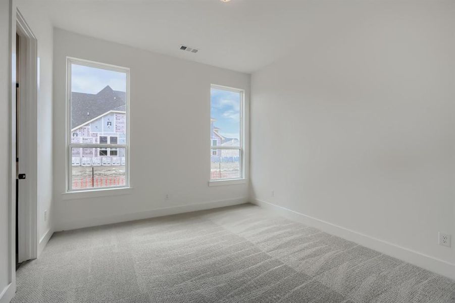 Spacious room featuring neutral paint, gray patterned carpet, and dual windows Spacious room featuring neutral paint, gray patterned carpet, and dual windows