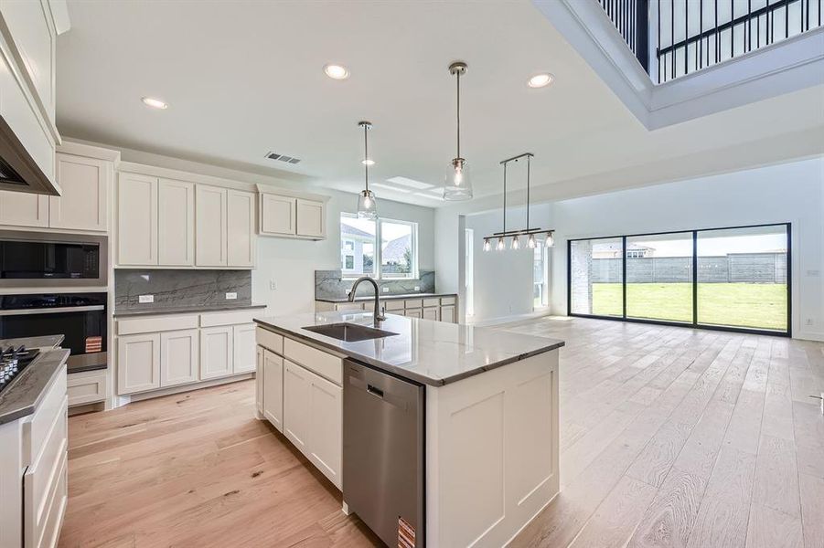 Kitchen with stainless steel appliances, a sink, custom exhaust hood, backsplash, and light wood finished floors Kitchen with stainless steel appliances, a sink, custom exhaust hood, backsplash, and light wood finished floors