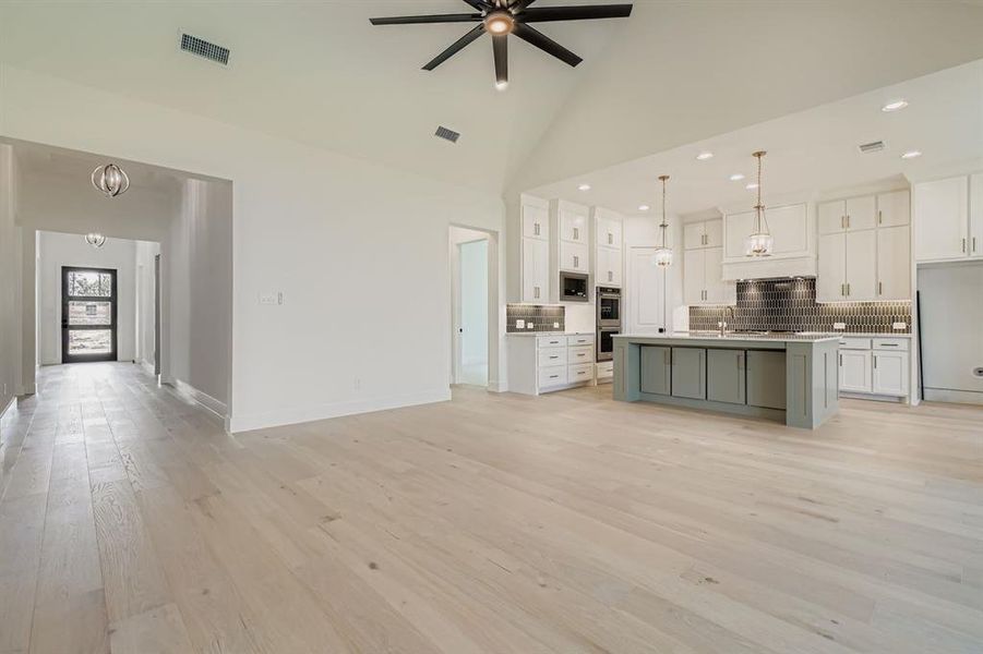 Unfurnished living room featuring light wood-style floors, high vaulted ceiling, a chandelier, recessed lighting, and a ceiling fan Unfurnished living room featuring light wood-style floors, high vaulted ceiling, a chandelier, recessed lighting, and a ceiling fan