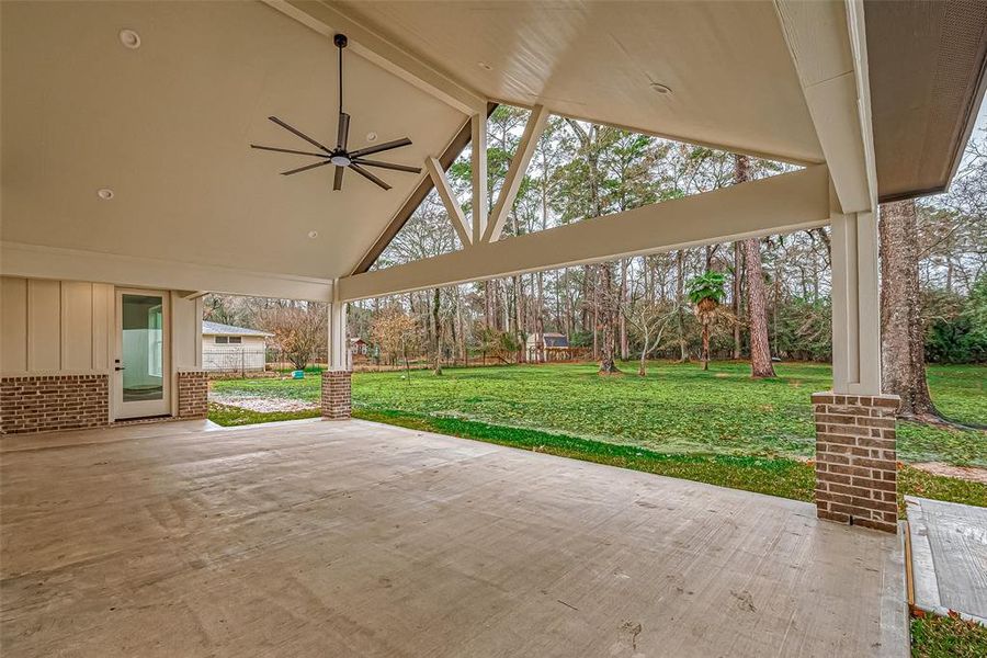 Spacious covered patio with a high vaulted ceiling and a large fan, overlooking an acre backyard with mature trees, perfect for outdoor relaxation and entertainment.