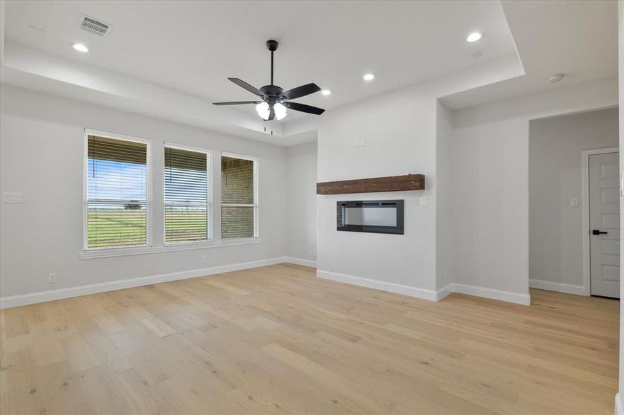 Unfurnished living room featuring light wood-style floors, a glass covered fireplace, visible vents, and recessed lighting