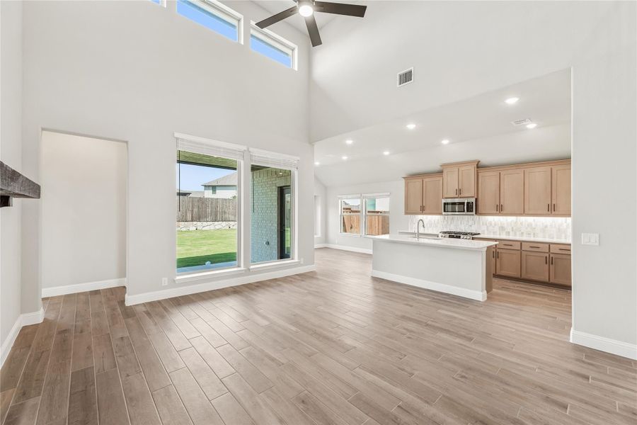 Open living area with vaulted ceiling and kitchen featuring wood cabinets, island, and hardwood floors