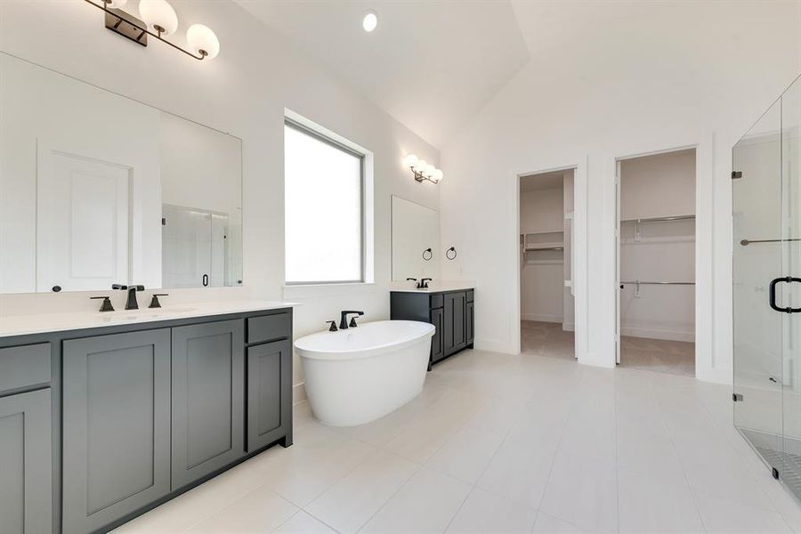 Full bathroom with a walk in closet, a stall shower, two vanities, a freestanding bath, and vaulted ceiling Full bathroom with a walk in closet, a stall shower, two vanities, a freestanding bath, and vaulted ceiling