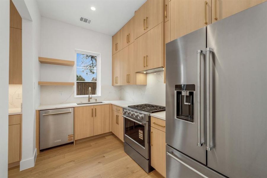 Kitchen with stainless steel appliances, light brown cabinetry, open shelves, modern cabinets, and light wood-type flooring
