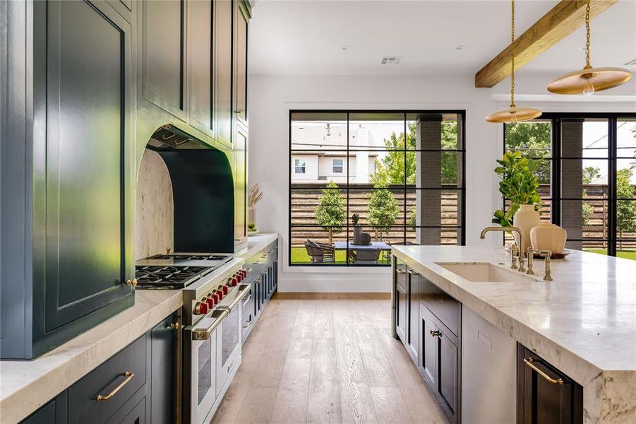 Kitchen with beamed ceiling, range with two ovens, light wood-type flooring, decorative light fixtures, and sink