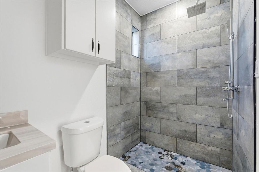 Moody gray and blue tones define this hall bathroom, featuring a modern exposed shower system and soft natural light from a peekaboo window.