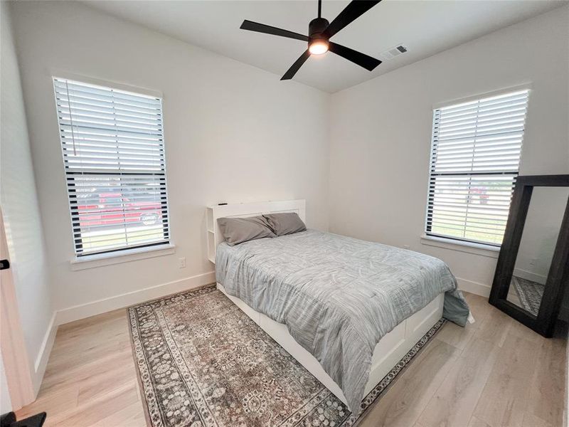 Bedroom with light wood-type flooring, a ceiling fan, and multiple windows