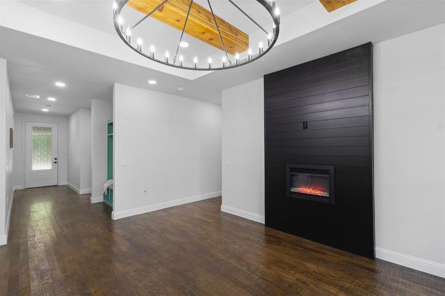 Unfurnished living room featuring wood finished floors, a large fireplace, recessed lighting, a tray ceiling, and a chandelier Unfurnished living room featuring wood finished floors, a large fireplace, recessed lighting, a tray ceiling, and a chandelier