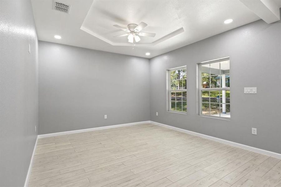 Spare room featuring a ceiling fan, light wood-type flooring, a tray ceiling, and recessed lighting