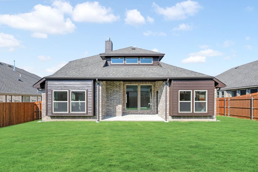 Rear view of single-story brick home with dark siding, covered patio, and fenced backyard lawn.